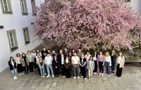 Gruppenfoto der neuen Nachwuchskräfte der Regierung der Oberpfalz beim Kennenlerntag im April 2026. Die Teilnehmenden stehen im Innenhof der Regierung vor einem großen rosa blühenden Baum.