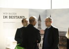 Gäste bei der Ausstellungseröffnung mit Ausstellung im Hintergrund