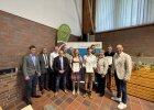 Gruppenfoto mit vier jungen Absolventinnen und Absolventen, die ihre Urkunden halten, sowie mehreren Ehrengästen und Offiziellen vor dem Roll-Up der Regierung der Oberpfalz. Aufnahme bei der Freisprechungsfeier in Weiden/Almesbach.