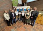 Gruppenfoto der drei besten Absolventen mit ihren Gutscheinen, flankiert von mehreren Ehrengästen und Offiziellen. Im Hintergrund ein Roll-Up der Regierung der Oberpfalz. Aufnahme bei der Freisprechungsfeier 2025 in Weiden/Almesbach.