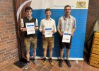 Drei junge Männer in Tracht halten ihre Gutscheine für besondere Leistungen vor einem Roll-Up der Regierung der Oberpfalz. Sie zählen zu den besten Absolventen der landwirtschaftlichen Ausbildung 2025 in der Oberpfalz.