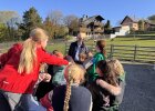 Kinder stehen in einer Gruppe im Freien um Walter Jonas und Erlebnisbäuerin Heidi Ziegaus auf dem Bauernhof.