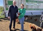 Walter Jonas und Heidi Ziegaus stehen vor einem Hühnerstall, Heidi Ziegaus hält ein Huhn auf dem Arm.