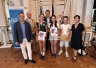 Vier Jugendliche des Erasmus-Gymnasiums Amberg stehen mit Urkunden und einem Preisumschlag gemeinsam mit Lehrkräften und Vertretern der Regierung der Oberpfalz.
