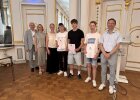 Drei Preisträger halten Urkunden und stehen mit Vertreterinnen und Vertretern von Regierung und Schule im Spiegelsaal.