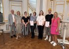 Drei Preisträgerinnen und Preisträger halten Urkunden und stehen mit Vertreterinnen und Vertretern von Regierung und Schule im Spiegelsaal.