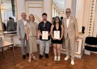 Zwei Preisträger des Beruflichen Schulzentrums Cham halten Urkunden und stehen mit Vertreterinnen und Vertretern von Regierung und Schule im Spiegelsaal.