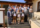 Drei ausgezeichnete Absolventinnen und Absolventen halten ihre Urkunden und stehen gemeinsam mit Ehrengästen auf einer Treppe.