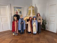 Regierungspräsident Walter Jonas und Regierungsvizepräsidentin Christiane Zürn stehen gemeinsam mit vier als Sternsinger verkleideten Kindern in einem historischen Raum der Regierung der Oberpfalz. Die Kinder tragen bunte Gewänder, Kronen und einen Stern.
