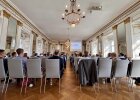 Blick von hinten in den Spiegelsaal der Regierung der Oberpfalz. Viele Personen sitzen in Stuhlreihen und hören einem Vortrag zu. Vorne ist eine Präsentationsleinwand zu sehen.