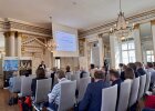 Teilnehmerinnen und Teilnehmer sitzen im Spiegelsaal der Regierung der Oberpfalz und verfolgen einen Vortrag. Auf der Leinwand ist eine Präsentation zur aktuellen Grundwassersituation in der Oberpfalz zu sehen.